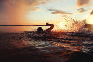 Athletic man is trained to swim in a lake at sunset. It flies a lot of water splashing. Vintage color